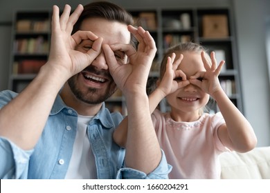 Portrait Of Overjoyed Young Father Have Fun With Cute Little Preschooler Daughter Relaxing Together At Home, Happy Dad Play With Small Girl Child, Make Funny Face Gestures, Enjoy Family Weekend