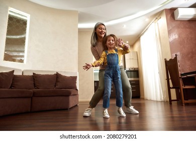 Portrait of overjoyed young girl with loose brown hair dancing together with active grandma. Young looking senior woman spending active time with her granddaughter at home. - Powered by Shutterstock