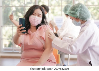 Portrait Of Overweight Asian Woman Selfie By Phone At While Getting Covid Vaccine In Clinic Or Hospital, With Hand Nurse Injecting Vaccine To Get Immunity From Virus. People Wearing Protective Mask.