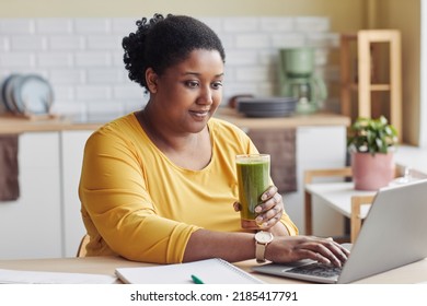 Portrait of overweight black woman drinking smoothie and using laptop at home - Powered by Shutterstock