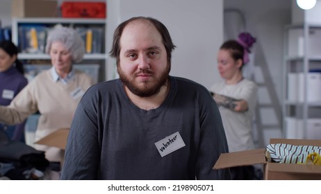 Portrait Of Overweight Male Volunteer Smiling At Camera Working In Military Donation Center With People Packing Donated Clothes In Boxes For Humanitarian Aid