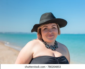 Portrait of overweight woman in black swimwear, hat and necklace at the sea