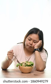 Portrait of overweight woman is tired of diet restrictions eating green salad sitting at table.