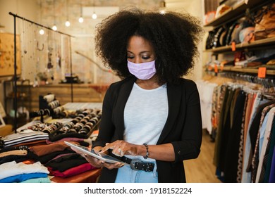 Portrait owner of clothing store at entrance of new business with tablet in hand analyze sales, new orders to be sent and check stocks wearing protective face mask during Coronavirus Covid-19 pandemic - Shutterstock ID 1918152224