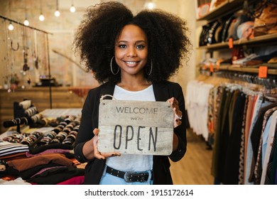 Portrait of the owner of the clothing store holding the sign with the words "Welcome we're open" in her hand to be attached to the window - Millennial woman welcomes customers at the entrance - Shutterstock ID 1915172614