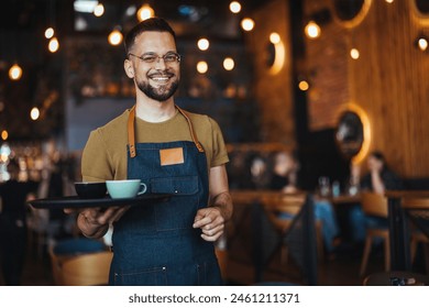 Portrait of Owner  Waiter at Restaurant. Portrait of handsome young male coffee shop owner standing at cafe. Portrait of a handsome barista in t-shirt and apron