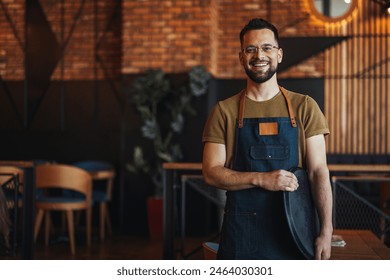 Portrait of Owner  Waiter at Restaurant. Portrait of handsome young male coffee shop owner standing at cafe. Portrait of a handsome barista in t-shirt and apron