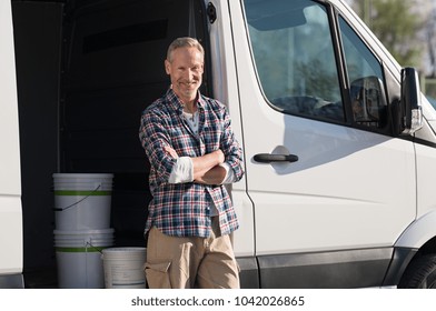 Portrait of painter standing next to his van with paint container. Decorator standing next to van and looking at camera. Happy smiling worker leaning on his white truck with folded arms. - Powered by Shutterstock