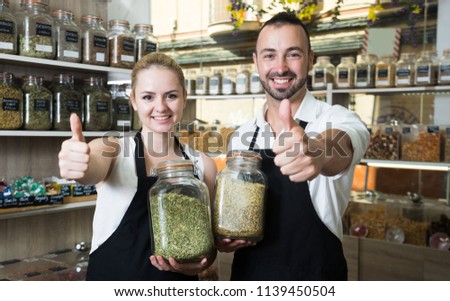 portrait of pair of charming sellers with aprons at store of herbs and ecological food