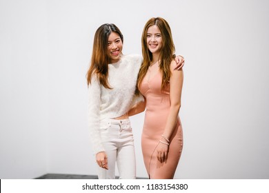 Portrait of a pair of young women friends holding one another to take a photograph together. They are both Chinese Asian, young and attractive. One is wearing a peach dress and the other a sweater. - Shutterstock ID 1183154380
