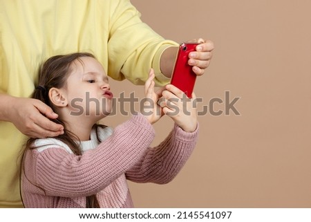 Portrait of parent taking smartphone away from girls hands, beige background. Dissatisfied daughter hold tight phone and resist. Concept of prevention of telephone addiction in children, nomophobia.