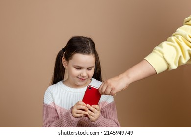 Portrait Of Parent Taking Smartphone Out From Girls Hands, Beige Background. Smiling Daughter Hold Phone And Fight Back. Concept Of Prevention Of Telephone Addiction In Children, Nomophobia.