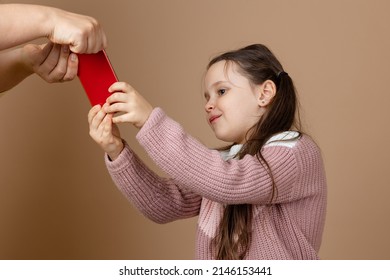 Portrait Of Parent Taking Smartphone Out From Girls Hands, Beige Background. Pleased Daughter Hold Phone And Fight Back. Concept Of Prevention Of Telephone Addiction In Children, Nomophobia.