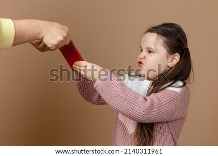 Portrait of parent taking smartphone out from girls hands, beige background. Discontent daughter hold tight phone and oppose. Concept of prevention of telephone addiction in children, nomophobia.
