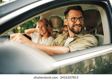 Portrait of a parents and their two daughters sitting in the car and driving away for the weekend to spend quality time together. Focus on a father driving a car and looking trough a window. - Powered by Shutterstock