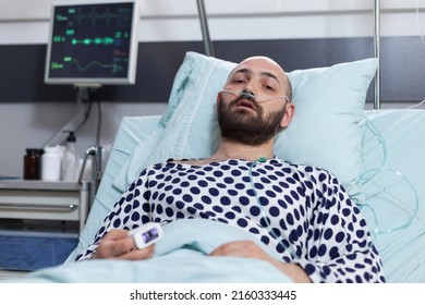 Portrait Of Patient With Breathing Problems Recieving Treatment Connected To Pulse Oximeter And Central Line Catheter Lying In Hospital Bed. Man Recovering After Surgery Treated With Intravenous