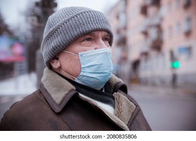 Portrait of  pensioner man on   street in winter during   coronavirus in medical mask .