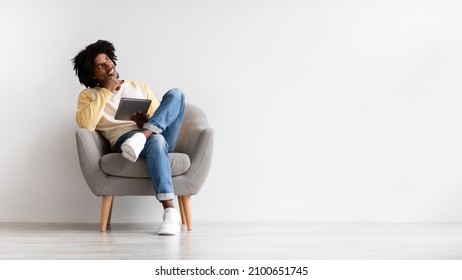 Portrait Of Pensive African American Guy Sitting In Chair With Digital Tablet, Thoughtful Young Black Man Making Online Shopping With Tab Computer, Choosing Options, Panorama With Copy Space