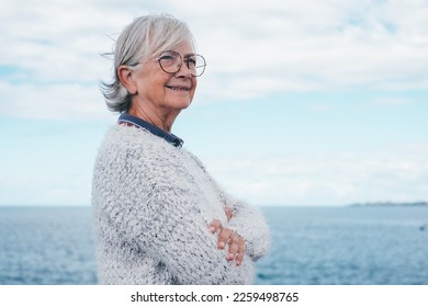 Portrait of pensive handsome senior woman standing by the sea looking away. Smiling elderly white-haired lady in outdoor excursion enjoying freedom, relax and retirement - Powered by Shutterstock