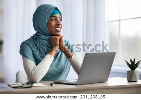 Portrait Of Pensive Happy Black Muslim Woman In Hijab Sitting At Desk With Laptop In Home Office, Islamic Lady Looking Away With Glad Face Expression, Thinking About Business Strategy, Copy Space