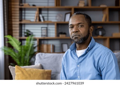 Portrait of a pensive middle-aged African American man sitting on a couch at home, looking reflective and serene. - Powered by Shutterstock