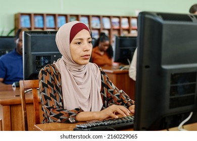 Portrait of pensive Muslim woman wearing hijab sitting in university library texting something on desktop computer - Shutterstock ID 2160229065