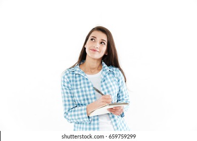 Portrait of a pensive pretty woman making notes in notepad and looking away at copy space isolated over white background