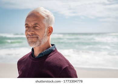 Portrait Of Pensive Senior Man At Beach Looking Away. Proud And Satisfied Old Man In Casual Enjoying Summer Holiday At Beach. Mature Retired Man Contemplating At Sea: IImagination And Future Concept.