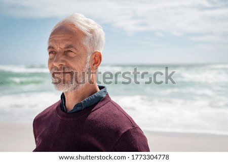 Portrait of pensive senior man at beach looking away. Proud and satisfied old man in casual enjoying summer holiday at beach. Mature retired man contemplating at sea: iImagination and future concept.
