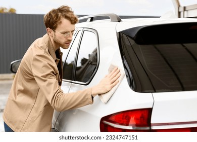 Portrait of pensive, serious man wearing glasses wiping down white SUV with microfiber cloth at self-service station. Concept of car washing, cleanliness, travel - Powered by Shutterstock