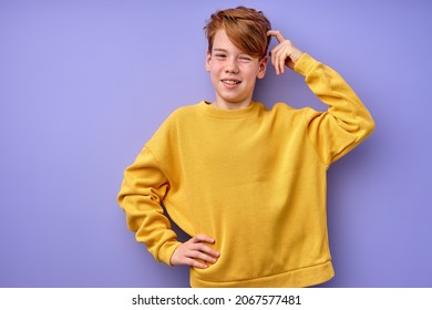 Portrait of pensive teen boy isolated on purple background. Thoughtful teenager holding hand on head, looking at camera. Beautiful caucasian funny child in shirt is thinking, in contemplation