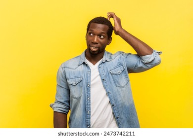 Portrait of pensive thoughtful man standing rubbing his head looking away with confusion thinking pondering, wearing denim casual shirt. Indoor studio shot isolated on yellow background. - Powered by Shutterstock