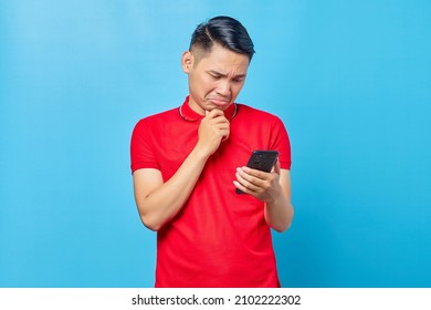 Portrait Of Pensive Young Asian Man Looking At Mobile Phone, Reading Fake News Isolated On Blue Background