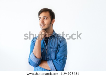 Portrait of pensive young Indian man in denim shirt holding chin. Handsome dark haired man thinking about new project. Startuper concept.