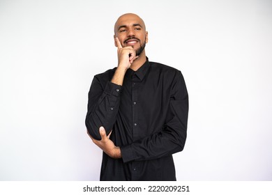 Portrait Of Pensive Young Man Leaning On Hand. Happy Latin American Male Model With Bald Head And Beard In Black Shirt Looking Away, Smiling And Touching Cheek. Contemplation, Focus Concept