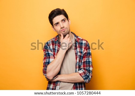Portrait of a pensive young man looking away at copy space isolated over yellow background