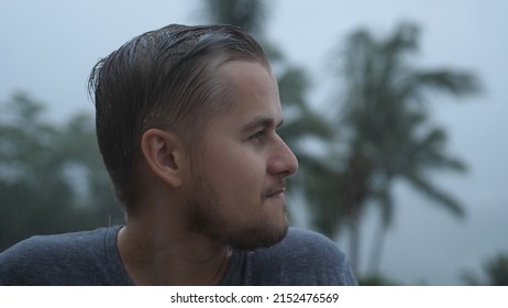 Portrait Of Pensive Young Man Standing In The Pouring Rain And Getting Soaked While Looking Into The Sky. Slow Motion