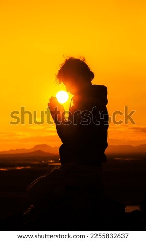 Portrait of a person praying with the sun between his hands and face. View in silhouette at sunrise time. Concept Religion and spiritual life