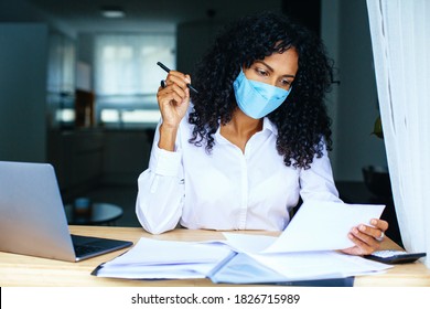 Portrait of a person working sitting at desk wearing mask, reading paper bill or contract - Powered by Shutterstock