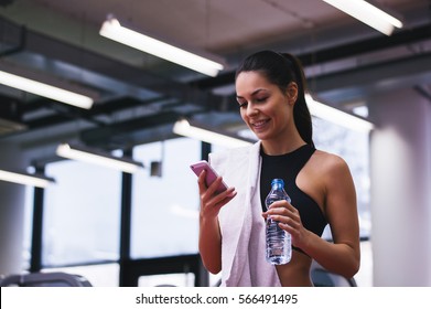 Portrait Of Personal Trainer Woman At Gym After Fitness Workout And Checking Sport App In Her Smartphone.