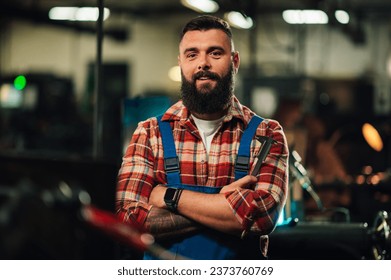 A portrait of a perspective young factory employee with a caliper in his hands. He has a beard and neat short hair, crossed arms with a tattoo. A confident metal worker is standing with arms crossed. - Powered by Shutterstock