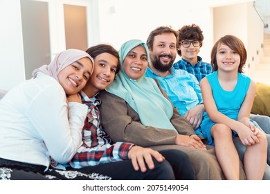 Portrait Photo Of An Arab Muslim Family Sitting On A Couch In The Living Room Of A Large Modern House. Selective Focus 