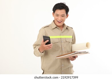 Portrait Photo Of An Asian Young Handsome Construction Worker, Holding Blue Print, In Working Uniform, Isolated On White Background