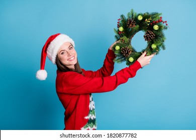 Portrait photo of girl wearing red xmas headwear hanging christmas handmade crafts wreath made of christmas tree branches decorative berries wooden cones isolated on blue color background