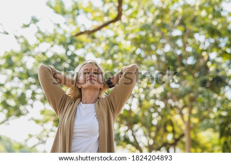 Portrait photo of happy senior Caucasian woman relaxing and breathing fresh air with sunlight in outdoors park. Elderly woman enjoying a day in the park on summer. Healthcare lifestyle and wellness 