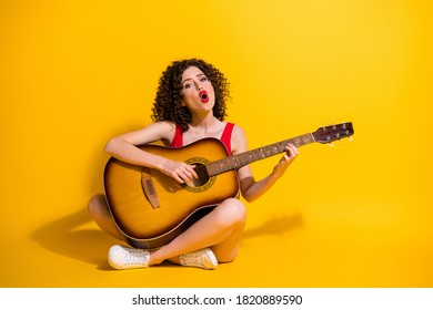 Portrait Photo Of Hipster Female Musician With Curly Hair Singing Vocal Voice Song Holding Keeping Playing Melody Guitar Chords Sitting Down Isolated On Vivid Yellow Color Background