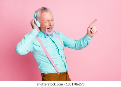 Portrait photo of old man listening to music with headphones singing favorite song pointing with finger isolated on pink color background - Powered by Shutterstock