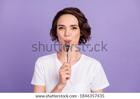 Portrait photo of slimming girl licking fork hungry diet wearing white t-shirt isolated on vibrant violet color background