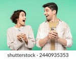 Portrait photo of smiling, shocked people holding mobile phones, looking each other, and screaming, isolated on a teal background. Online shopping concept