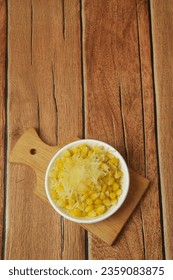 Portrait photo of some shaved corn sprinkled with sweet cheese and milk on a wooden table
